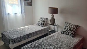 A room with two beds, a bedside table with a lamp, and a window with curtains. - Gîte "la Galinette" in village center, air-conditioned with swimming pool. (Vallon-Pont-d'Arc)