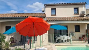 Area piscina con patio recintato, arredi da esterno e ombrelloni.