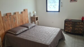 Una camera da letto con una testiera in legno, un letto con copripiumino decorato, un comodino con una lampada, una cassettiera e una finestra con motivo a foglia.