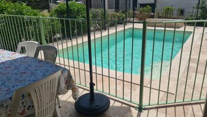 Una piscina con recinzione verde, un tavolo con tovaglia floreale e sedie.