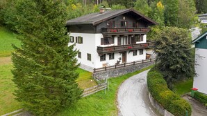 A multi-story building with a balcony, surrounded by greenery and a winding road. - Ferienhaus Höllbacher, Mountian View & Garden (Bad Gastein)
