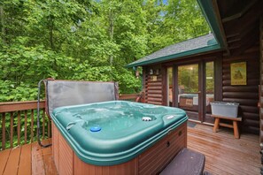 Ein Whirlpool auf einer Holzterrasse mit einer Hütte im Hintergrund, umgeben von Bäumen.