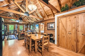 Ein Blockhaushaus-Interieur mit einem Holzesstisch, Stühlen, einem großen Holzschrank und einer Decke mit freiliegenden Balken und einer Pendelleuchte.