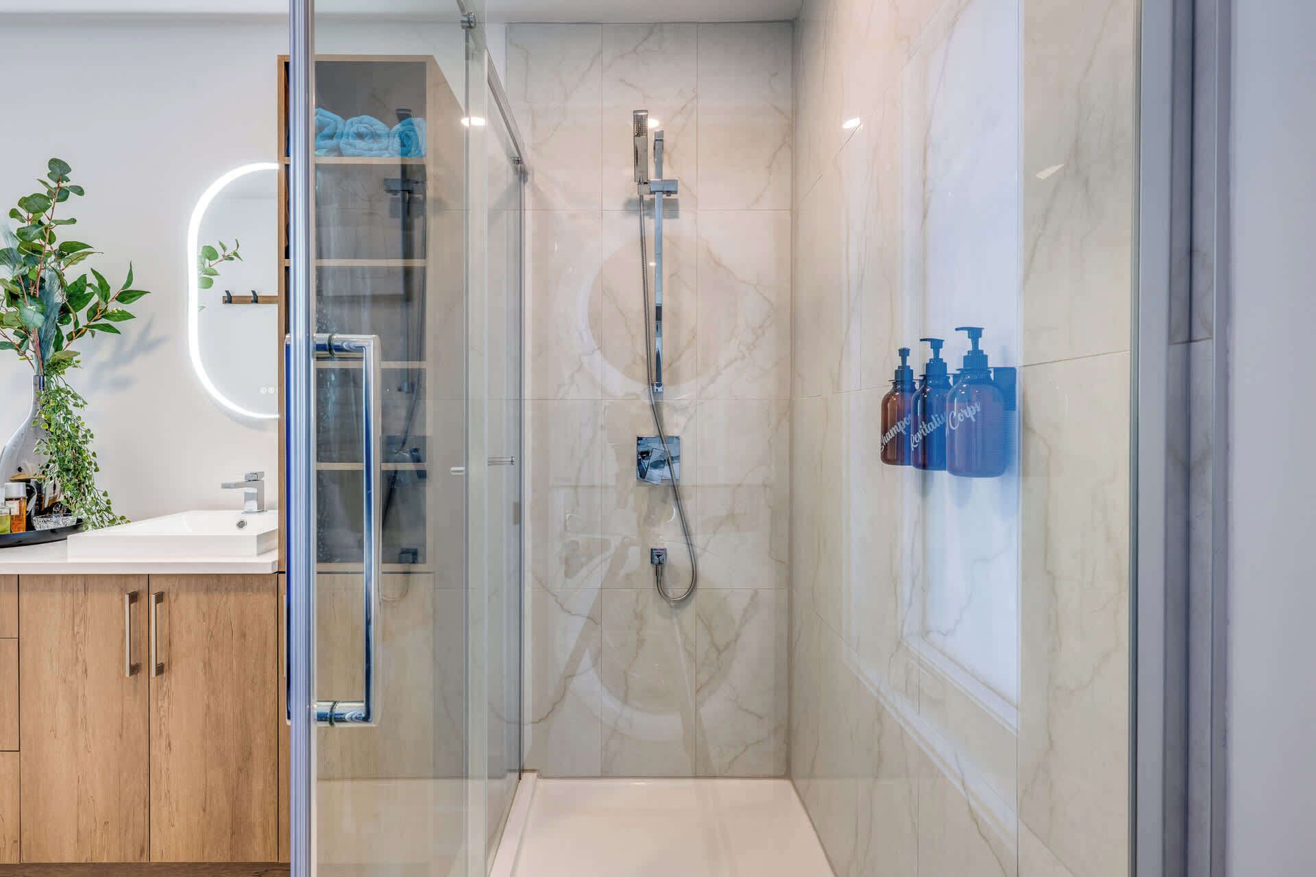 A modern bathroom with a glass-enclosed shower, a wooden vanity, and a marble-tiled wall.