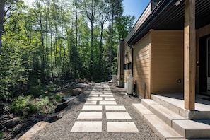 A pathway leading to a building with a modern design, surrounded by a forested area. - Private Pool & Spa | Chalet Bella Vista (Saint-Côme)
