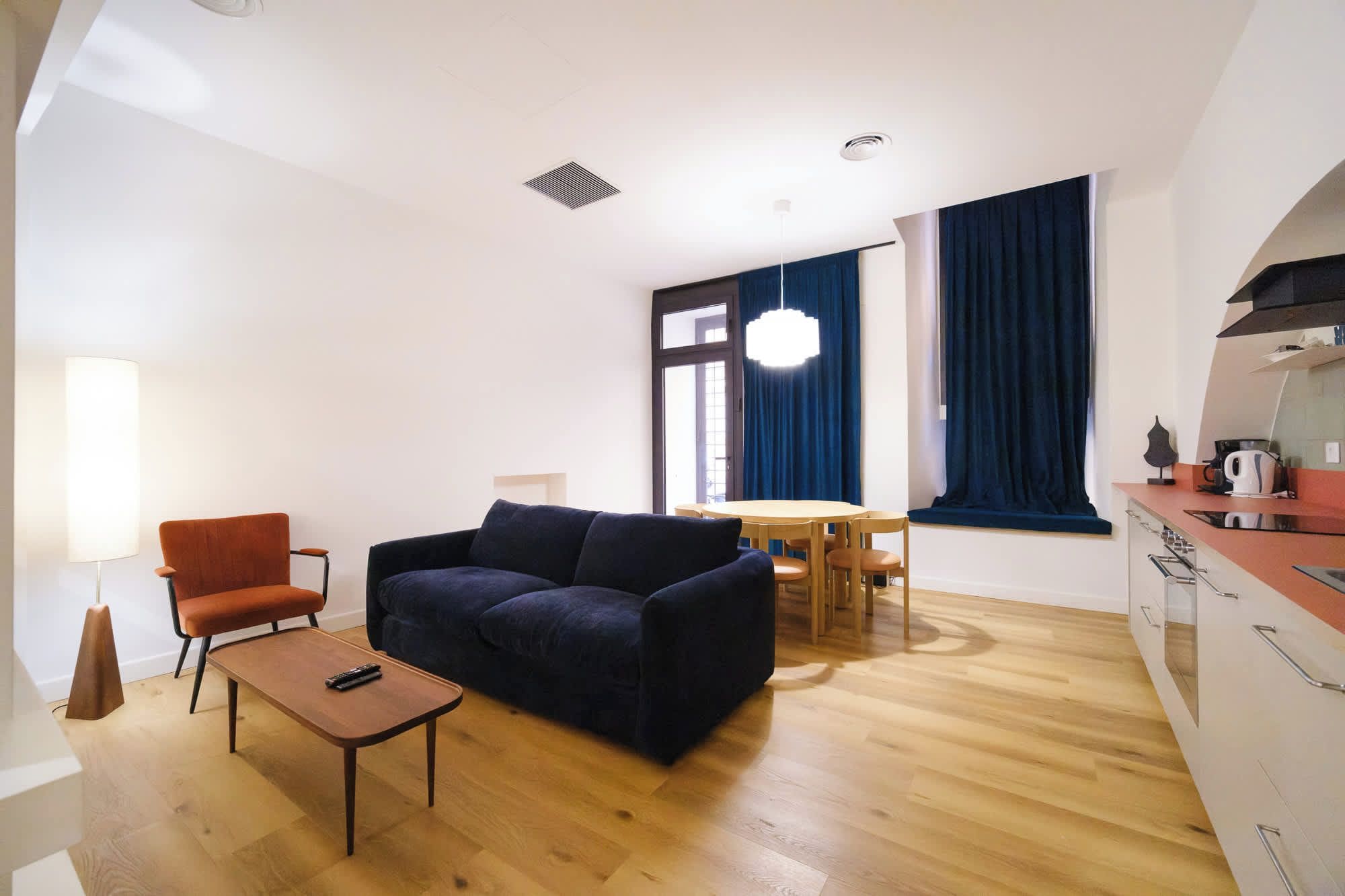 A modern living room with a sofa, a small table, and a dining area with a table and chairs.