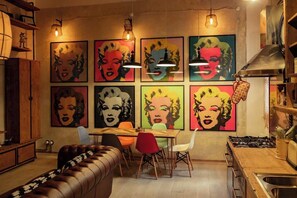 A modern kitchen with a dining area, featuring a brown leather couch, a wooden dining table, and colorful artwork on the walls. - BuddyRent - Lucky Jazz - Nomentana - 5 ospiti (Rome)