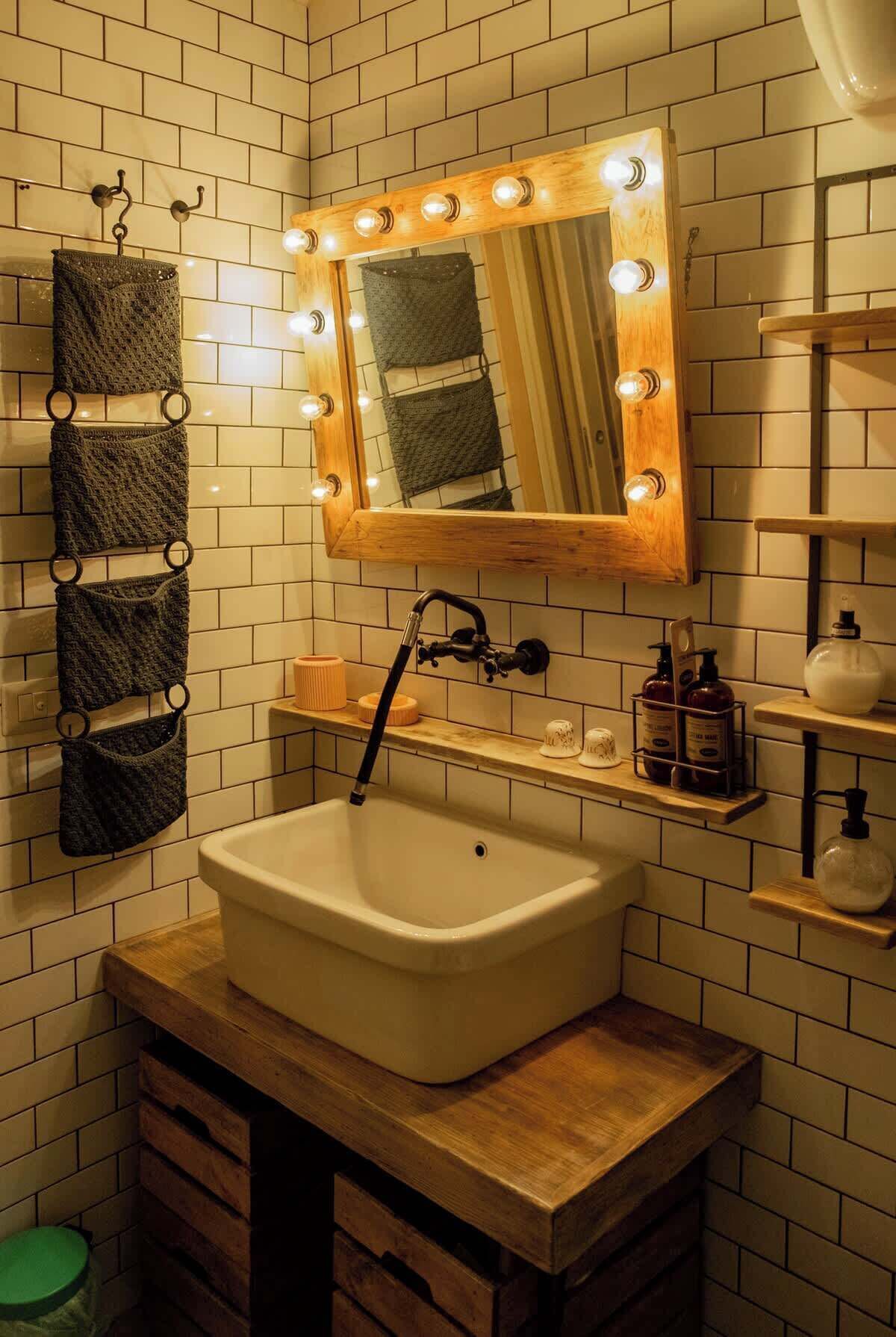 A bathroom with a white sink, a mirror with lights, a towel rack, and a shelf with toiletries.