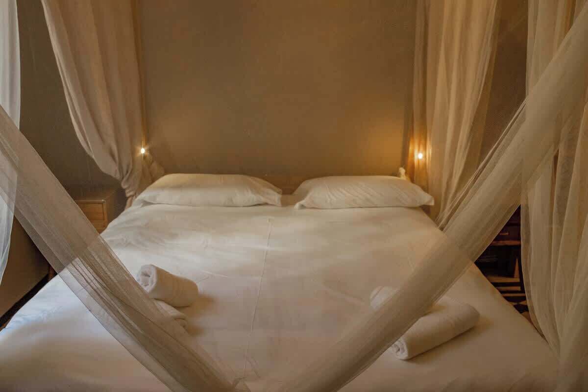 A bed with white linens, a rolled towel, and sheer curtains.