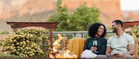 A couple sitting on a bench outdoors with a fire in the foreground.