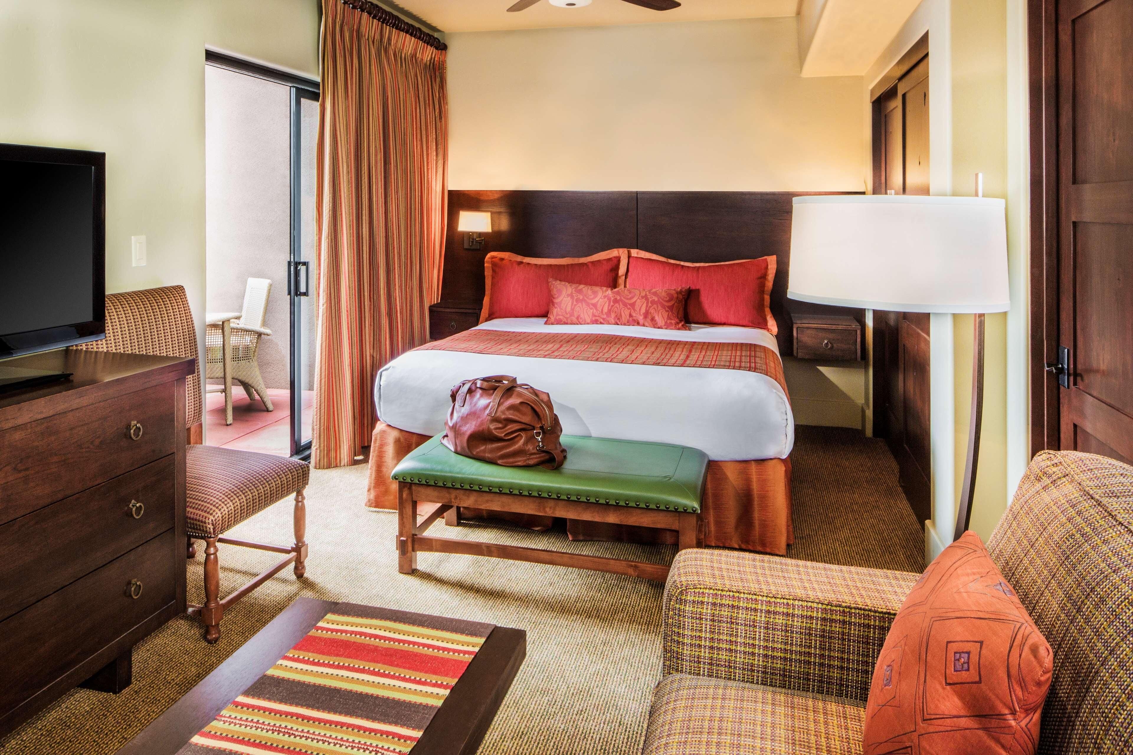A hotel room with a bed, a television, a desk, a chair, a bench, and a lamp.
