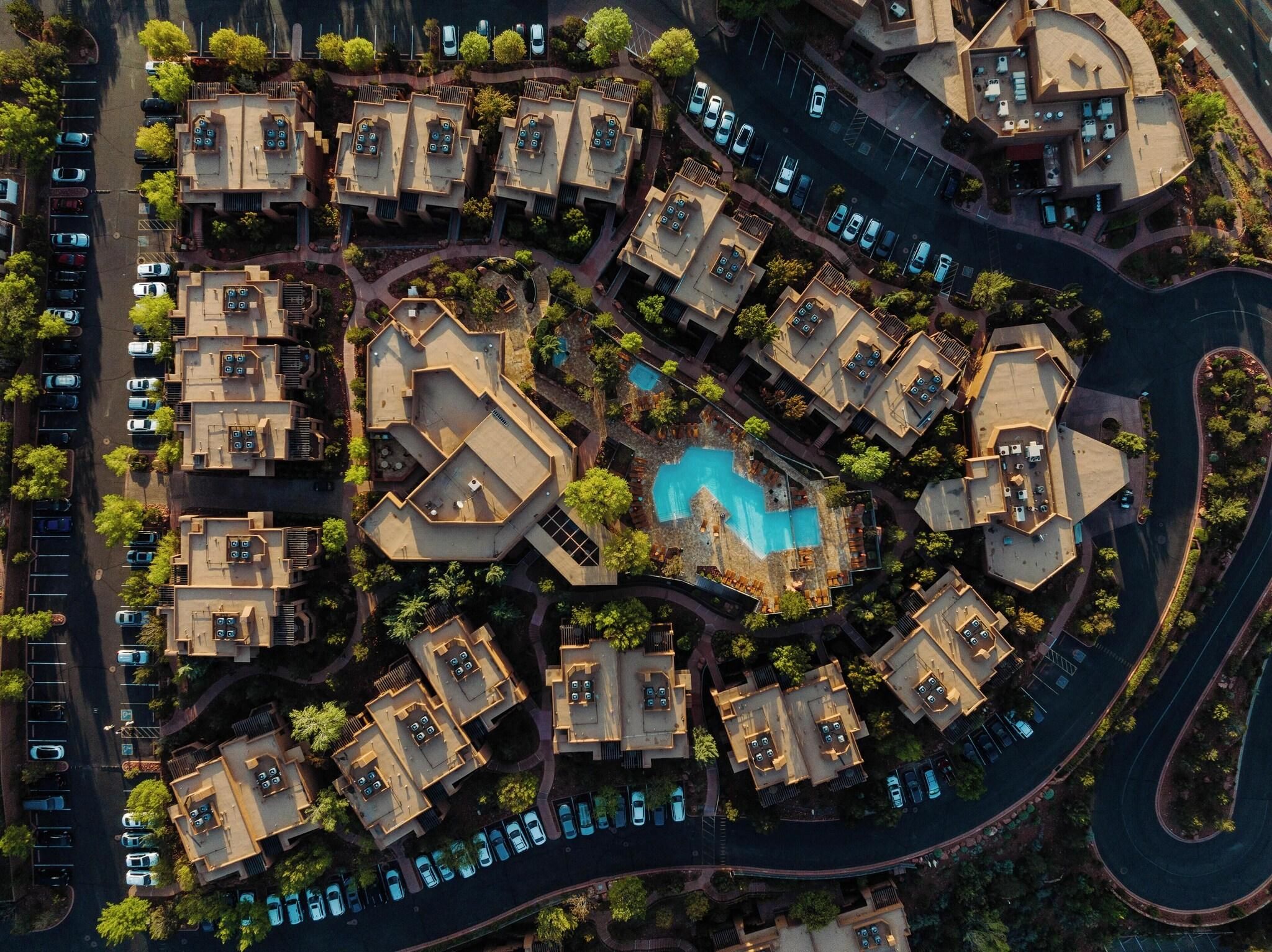 An aerial view of a residential complex with multiple buildings, a central swimming pool, and surrounding greenery.
