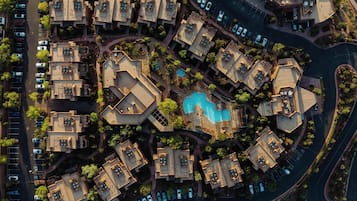 An aerial view of a residential complex with multiple buildings, a central swimming pool, and surrounding greenery.
