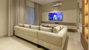 Uma sala de estar moderna com um sofá seccional, uma TV de tela plana montada e um aparelho de ar condicionado na parede.