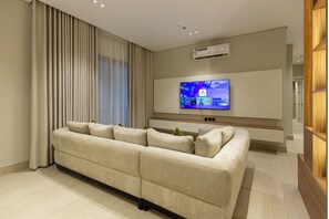 Ein modernes Wohnzimmer mit einer Eckcouch, einem wandmontierten Flachbildfernseher und einer Klimaanlage an der Wand.
