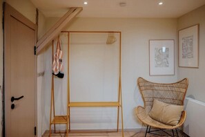 Ein Zimmer mit einer Holztür, einem Rattanstuhl, einem Metallständer und gerahmten Kunstwerken an der Wand.
