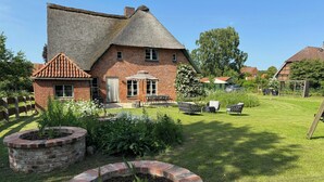 Ein Backsteinhaus mit Strohdach, ein Garten mit kreisförmigem Ziegelpflanztopf und eine Terrasse mit Gartenmöbeln.