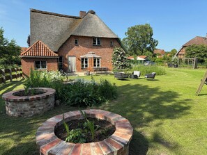 Ein Backsteinhaus mit Strohdach, ein Garten mit kreisförmigem Ziegelpflanztopf und eine Terrasse mit Gartenmöbeln.