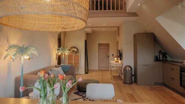 Ein modernes Interieur mit einer Couch, Hocker, Esstisch und einer Küchenzeile.