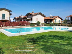 Ein Schwimmbad, umgeben von gepflegtem Rasen und einer Reihe von Häusern mit Balkonen.