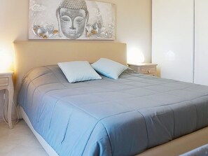 Ein Bett mit blauer Bettdecke, zwei Kissen und einem Wandbild darüber.