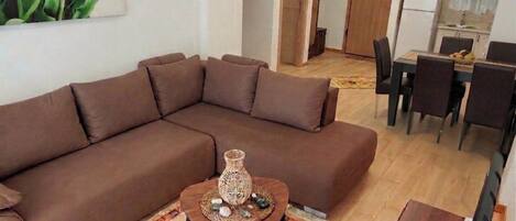 Un salon comprenant un canapé d’angle marron, une petite table en bois agrémentée d’objets décoratifs et un coin repas avec des chaises et une table.