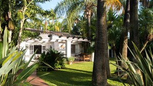 A white house with a tiled roof, surrounded by palm trees and a well-maintained lawn. - Villa in palm tree plantation, near the beach. (Marbella)