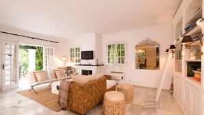 A spacious living room with a sofa, ottoman, and a television. - Villa in palm tree plantation, near the beach. (Marbella)
