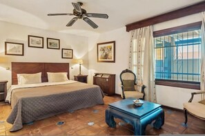A hotel room with a bed, a desk, a chair, a ceiling fan, and a window with curtains. - Grand Marbella Estate with tropical gardens (Marbella)