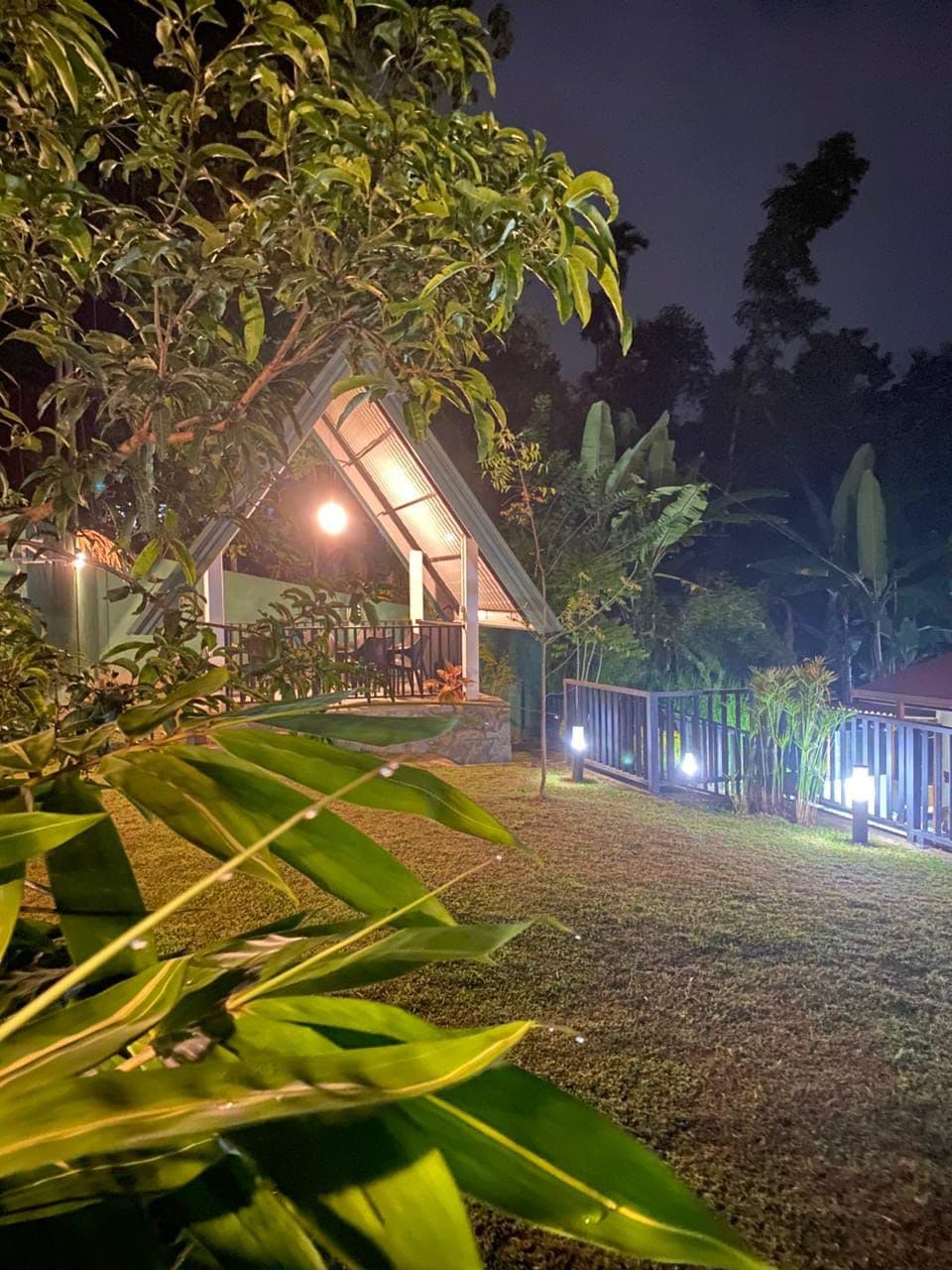 A building with a sloped roof, surrounded by greenery and a paved area.