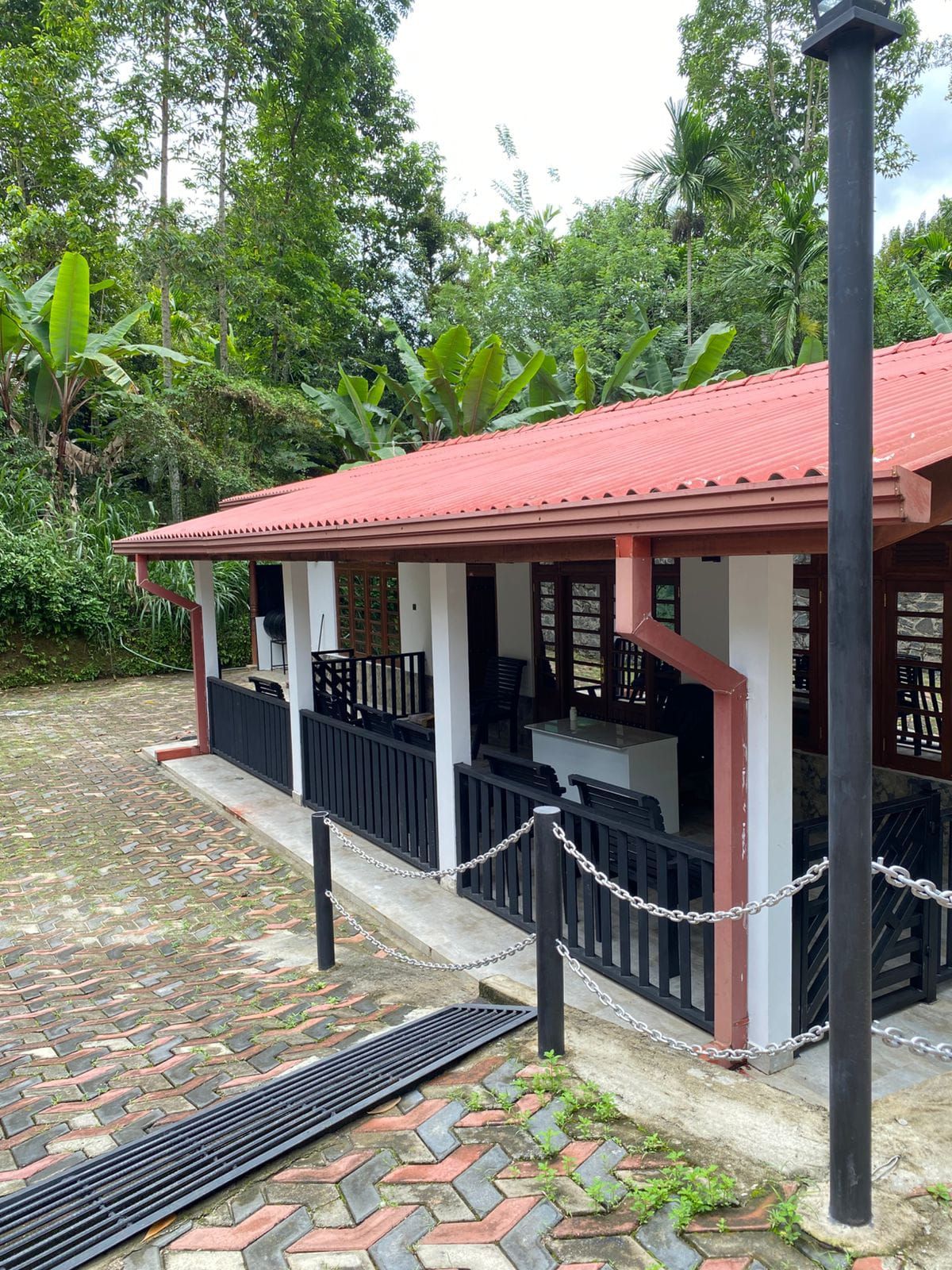 Un bâtiment avec un toit rouge, un patio couvert doté de sièges et une clôture en treillis métallique.