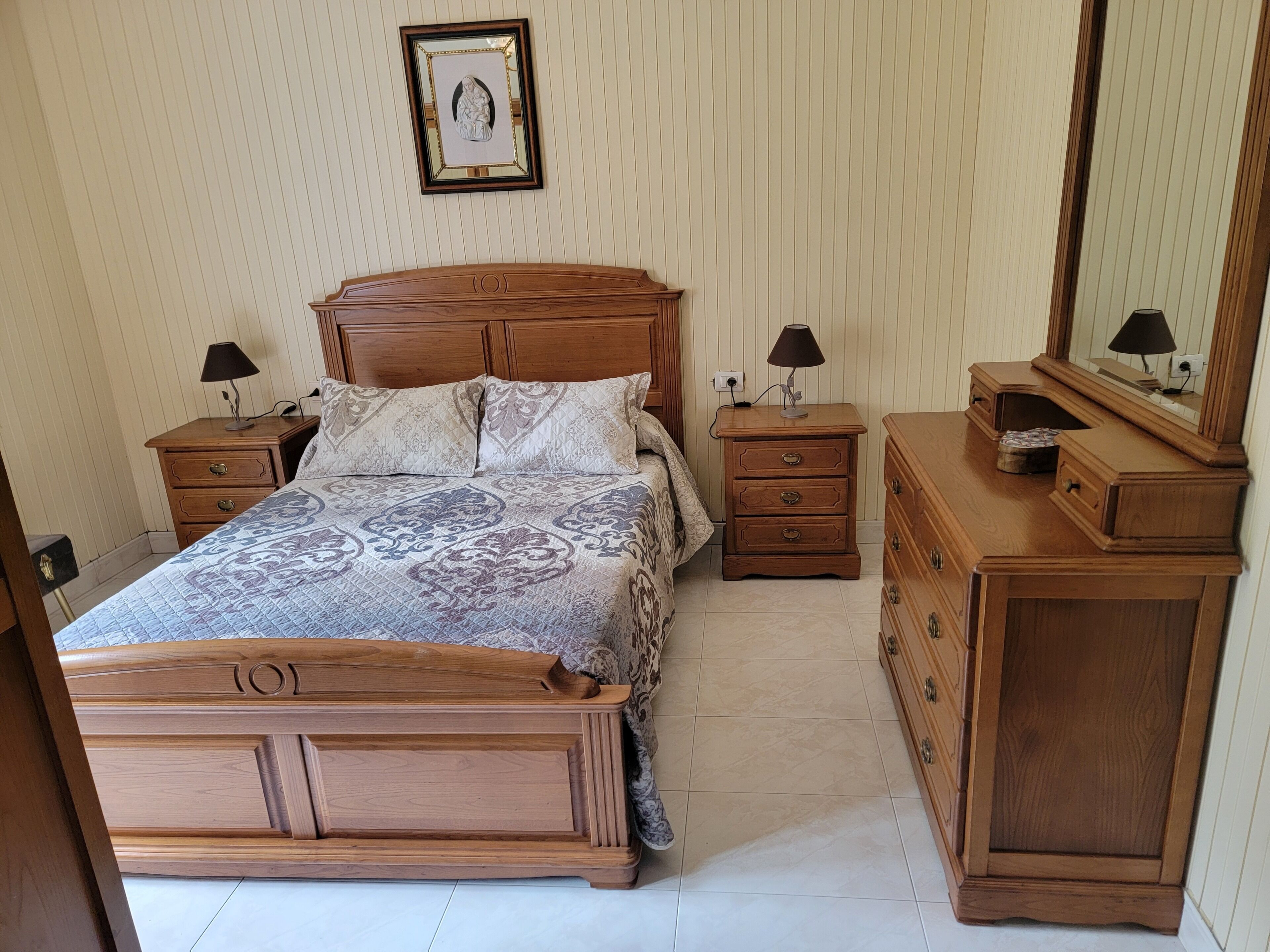 A bedroom with a wooden bed, two nightstands, a dresser, and a mirror.