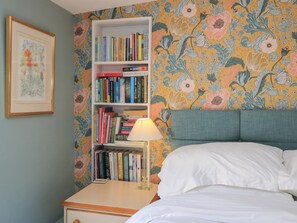 A bedroom with a bed, a bedside table, a lamp, and a bookshelf against a floral wallpaper. - 4 Duck Street (Dorchester)