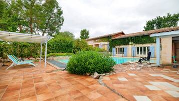 Propiedad residencial con piscina, mobiliario exterior y zona de patio techada.