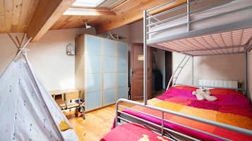 Una cama individual superpuesta con colcha colorida, un armario de madera, una mesita y una estructura similar a una tienda de campaña.