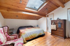 Une chambre avec un puits de lumière, un plafond en bois, un lit recouvert d’une courtepointe colorée, une commode et une chaise.
