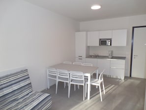 Ein gemütlicher Wohnbereich mit Esstisch und Stühlen, einer Küchenzeile und einem gestreiften Sofa.