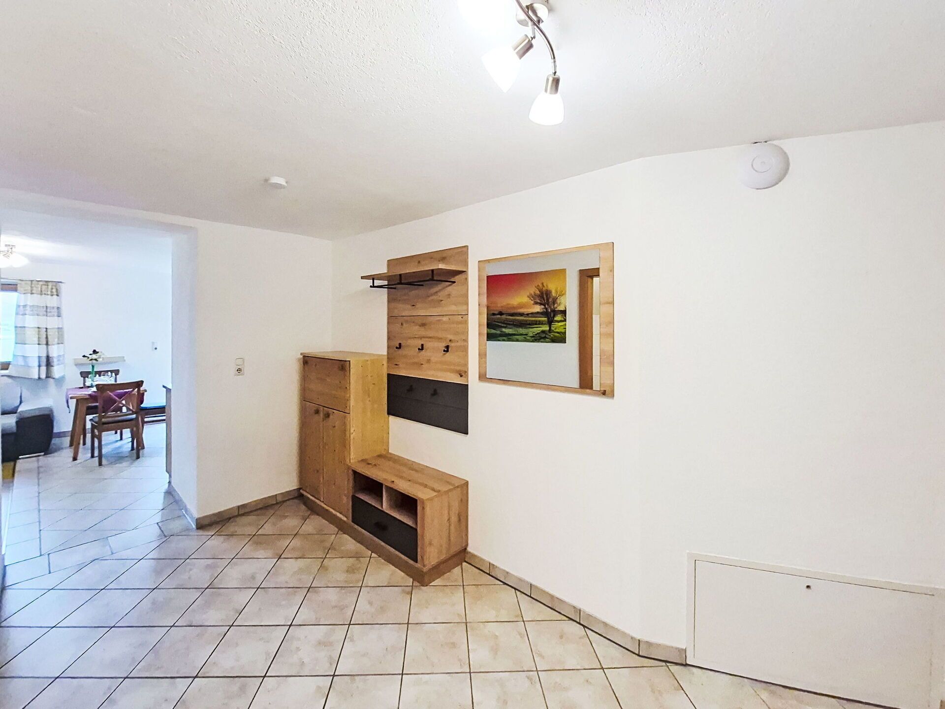 Une pièce avec un meuble en bois, une étagère fixée au mur, un cadre photo et un luminaire au plafond.