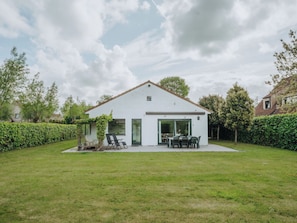 A white two-story house with a patio, a dining area, and a garden.