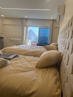 Een hotelkamer met twee bedden, uitzicht op een piramide en een balkon met stoelen.