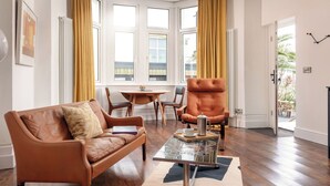 A modern living room with a leather sofa, a tufted armchair, a glass coffee table, and a dining area with a table and chairs. - Beautiful apartment for 2 people with A/C, WIFI, TV and pets allowed (Falmouth)