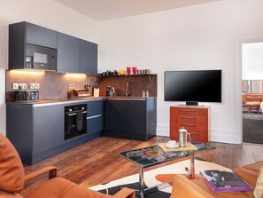Un espace de vie compact comprenant un coin cuisine, un téléviseur à écran plat, une table basse et un canapé.