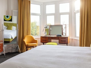 Ein Hotelzimmer mit einem Bett, einem Schreibtisch mit Spiegel, einem Stuhl und einem fenster mit Vorhängen.