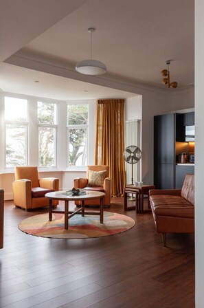 Ein geräumiges Wohnzimmer mit großem Fenster, runden Couchtisch, Ledersofas und einer Stehlampe.