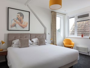 Ein Schlafzimmer mit einem Bett, einem gelben Sessel, einem Fenster mit Aussicht und einem gerahmten Kunstwerk an der Wand.