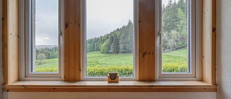 Una habitación con un banco, dos ventanas con marcos de madera y vista a un paisaje verde.