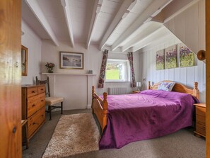 Ein Schlafzimmer mit einem Bett, einem Holzkoffer, einem Stuhl und einem Fenster mit Vorhängen.