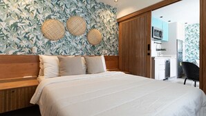 A bedroom with a large bed, a wooden headboard, a wall with a leafy pattern, and a sliding door leading to a kitchenette. - Colonial Studio·Steps from Parque Colón |Yellowkey (Santo Domingo)