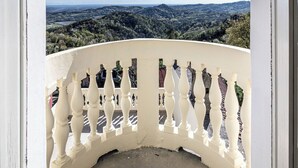 Ein Balkon mit weißer Brüstung, der auf eine hügelige Landschaft blickt.