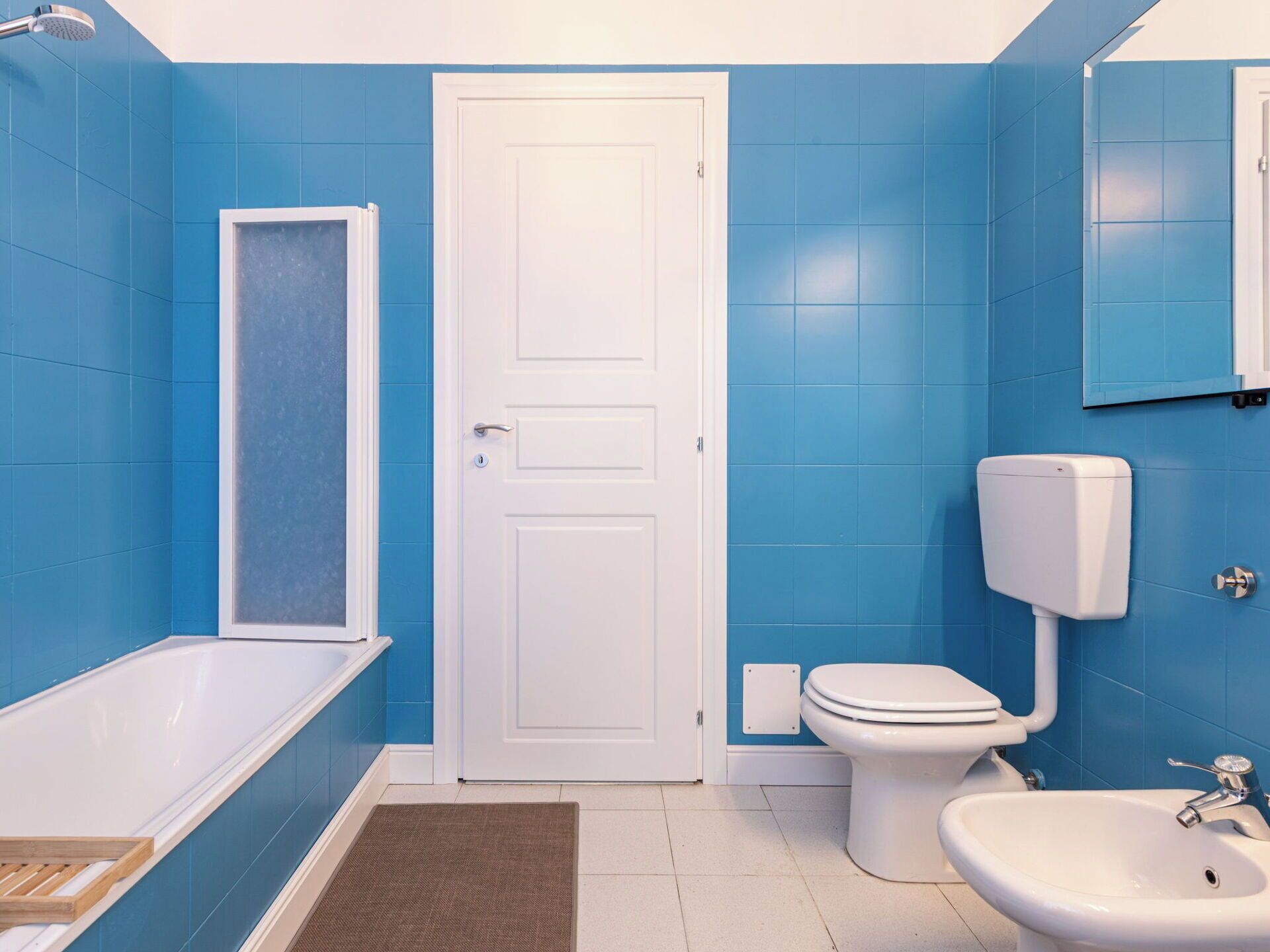 Ein Badezimmer mit blauen Fliesen, einer weißen Badewanne, einer Toilette und einem Waschbecken.